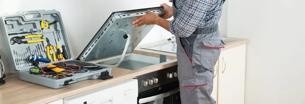 Cooktop repair technician lifting a built-in stovetop for service in Lakeland, FL