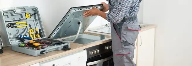 Cooktop repair technician lifting a built-in stovetop for service in Lakeland, FL