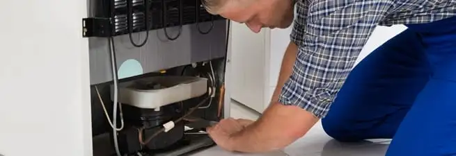 Refrigerator repair technician servicing the compressor and condenser area in Lakeland, FL