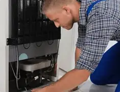 Refrigerator repair technician servicing the compressor and condenser area in Lakeland, FL